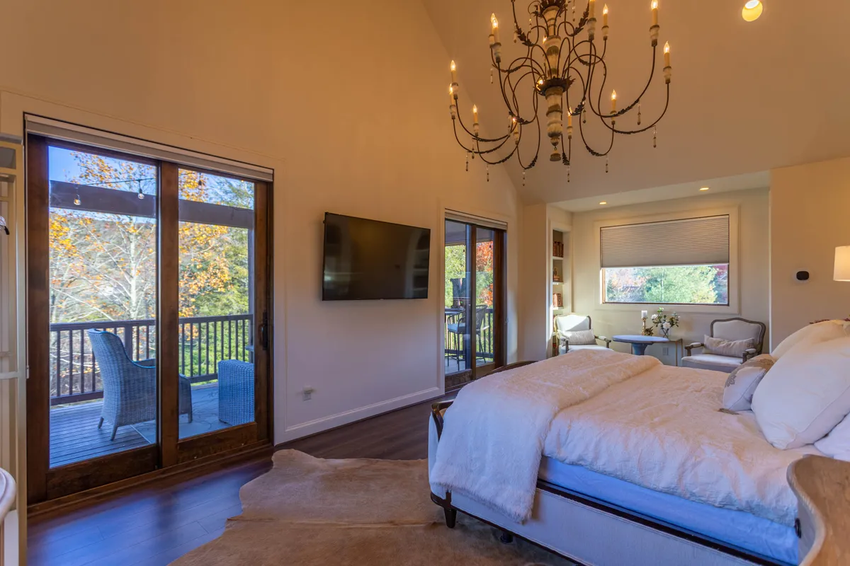 A king suite with a plush bed, chandelier, and sliding doors leading directly to a private balcony. A cozy seating area invites quiet moments, and the view from the balcony hints at mountain sunrises—perfect for morning coffee or evening relaxation.