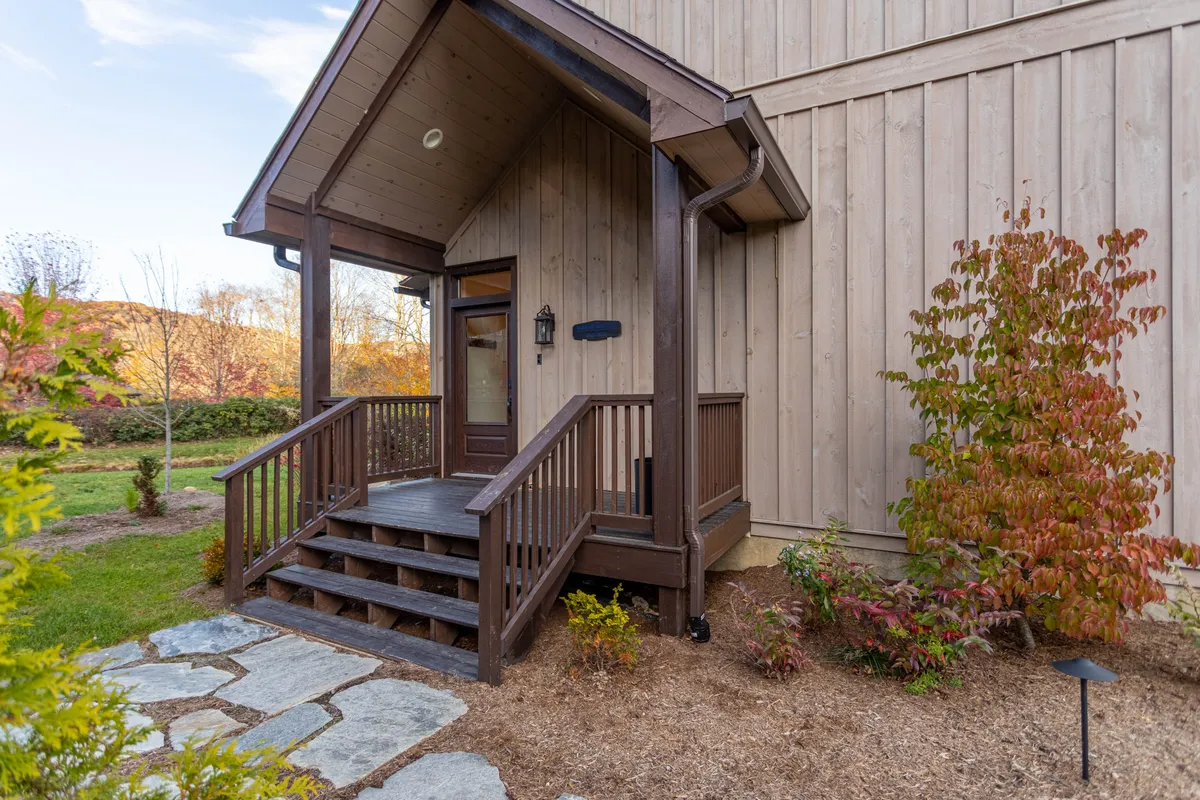 A welcoming view of the home's landscaped front entrance, complete with wooden steps, decorative shrubs, and a cozy porch. The garden hints at seasonal changes, while the overall atmosphere is inviting and tranquil, suggesting a warm return from outdoor adventures.