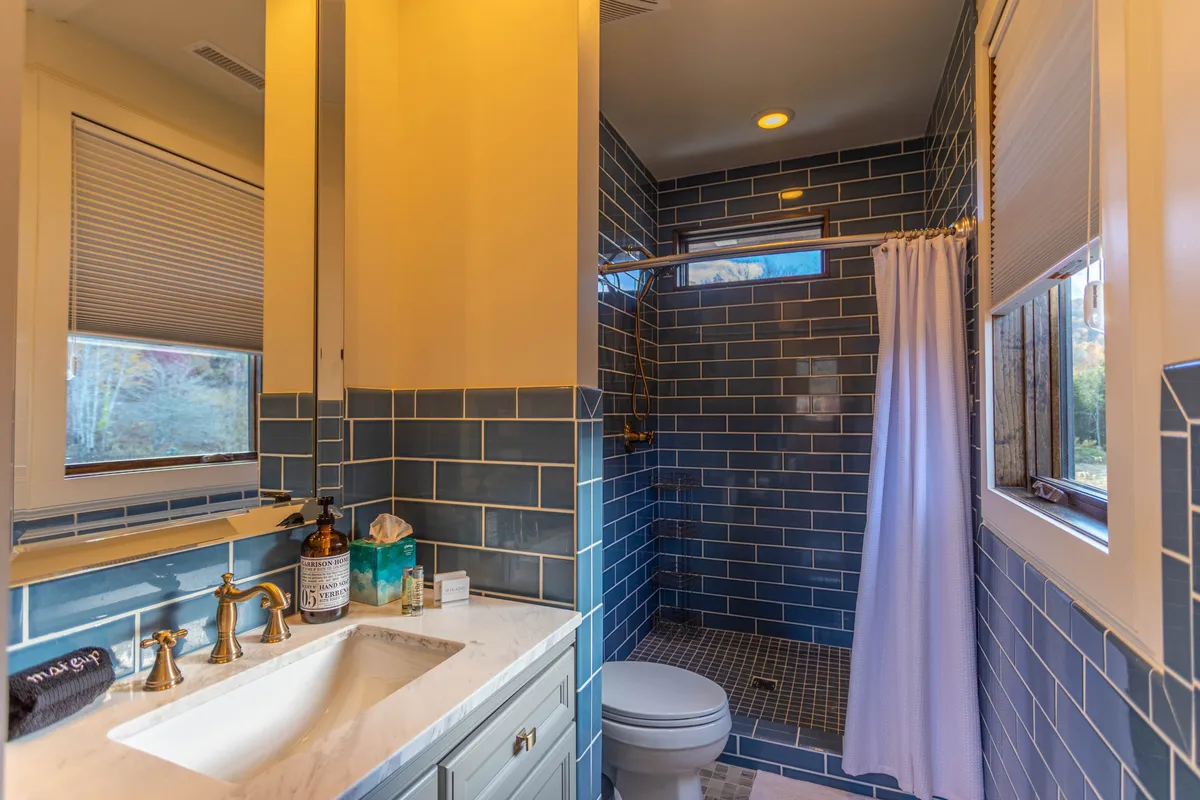 A luxury en-suite bathroom with striking blue tiled walls, marble countertops, and a walk-in shower. The space is well-lit and modern, evoking a spa-like feel ideal for unwinding after a day of adventure or preparing for an inspired morning.