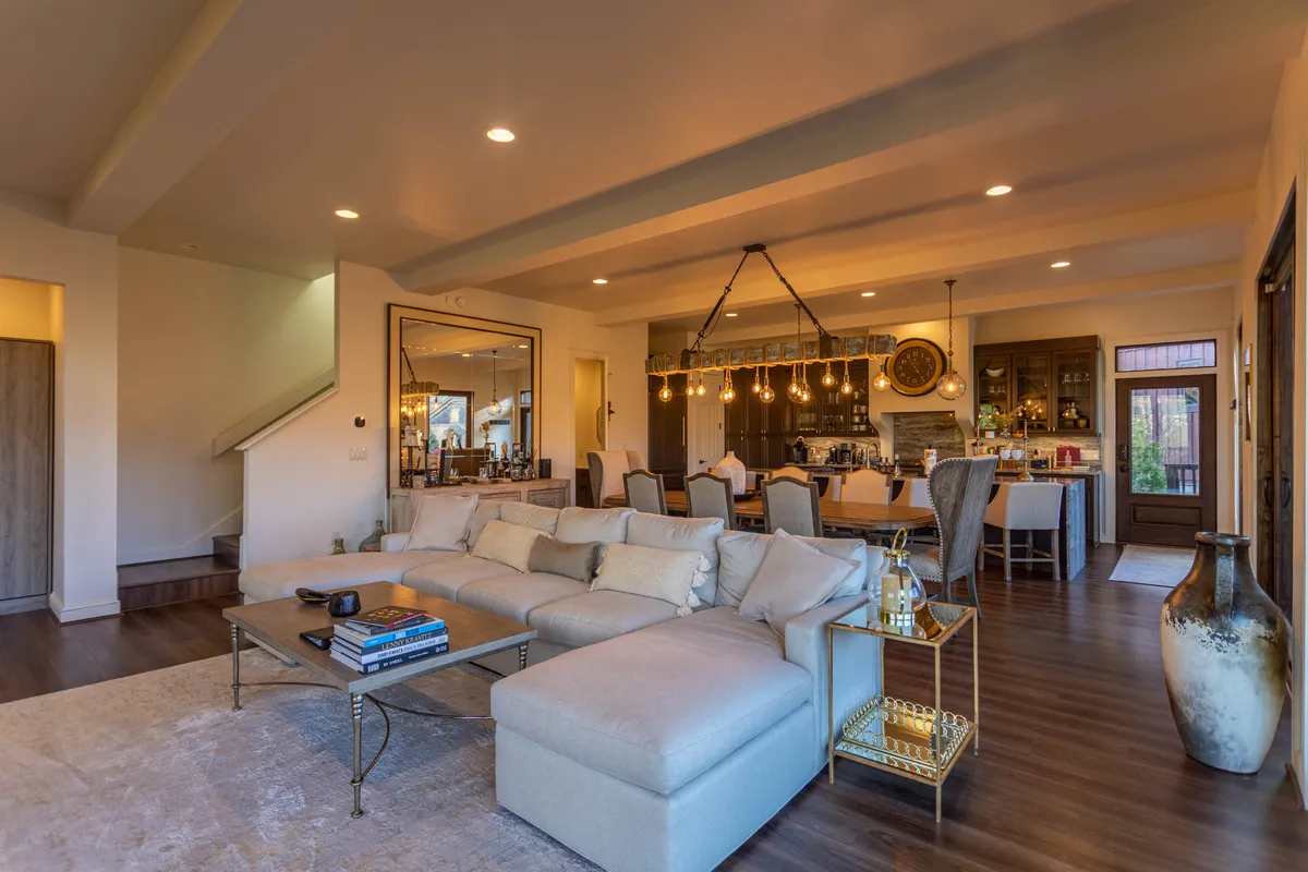 The open-concept living, kitchen, and dining area is depicted here, with the sectional sofa, kitchen island, and a dining table all visible in one frame. Decorative lighting and a large mirror enhance the sense of space, making it perfect for gatherings, shared meals, and family time.