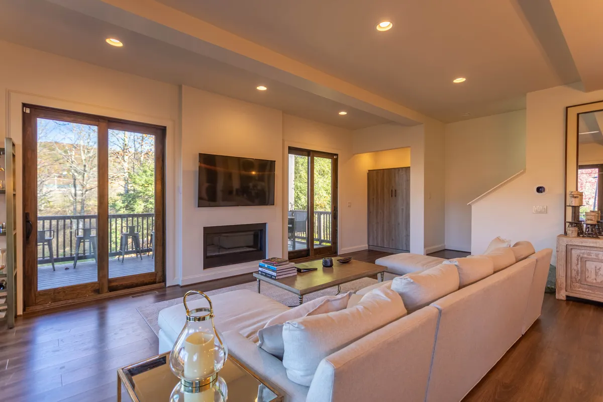 The open-concept living area is showcased here, featuring a plush sofa, coffee table, television, fireplace, and sliding glass doors that open to nature views. The space radiates warmth and invites families or friends to gather for relaxing evenings or movie nights after a day of exploration.
