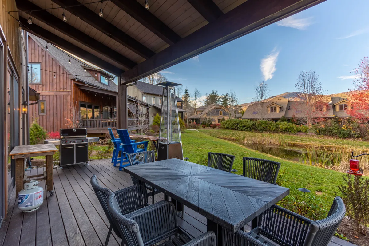 A backyard area featuring a large outdoor dining table, a grill, and a seating area set against a backdrop of a grassy lawn and a reflective pond. This setting is ideal for gatherings, with the pond as a focal point for morning or evening relaxation.